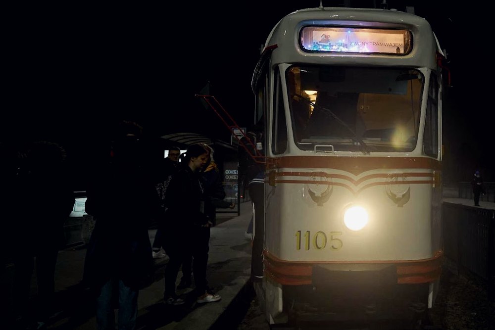 Uczestnicy wsiadający nocą do zabytkowego tramwaju na przystanku